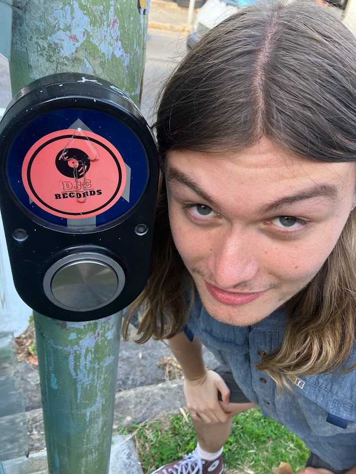 Dylan next to a sticker on a pedestrian button that reads 'DJC Records'